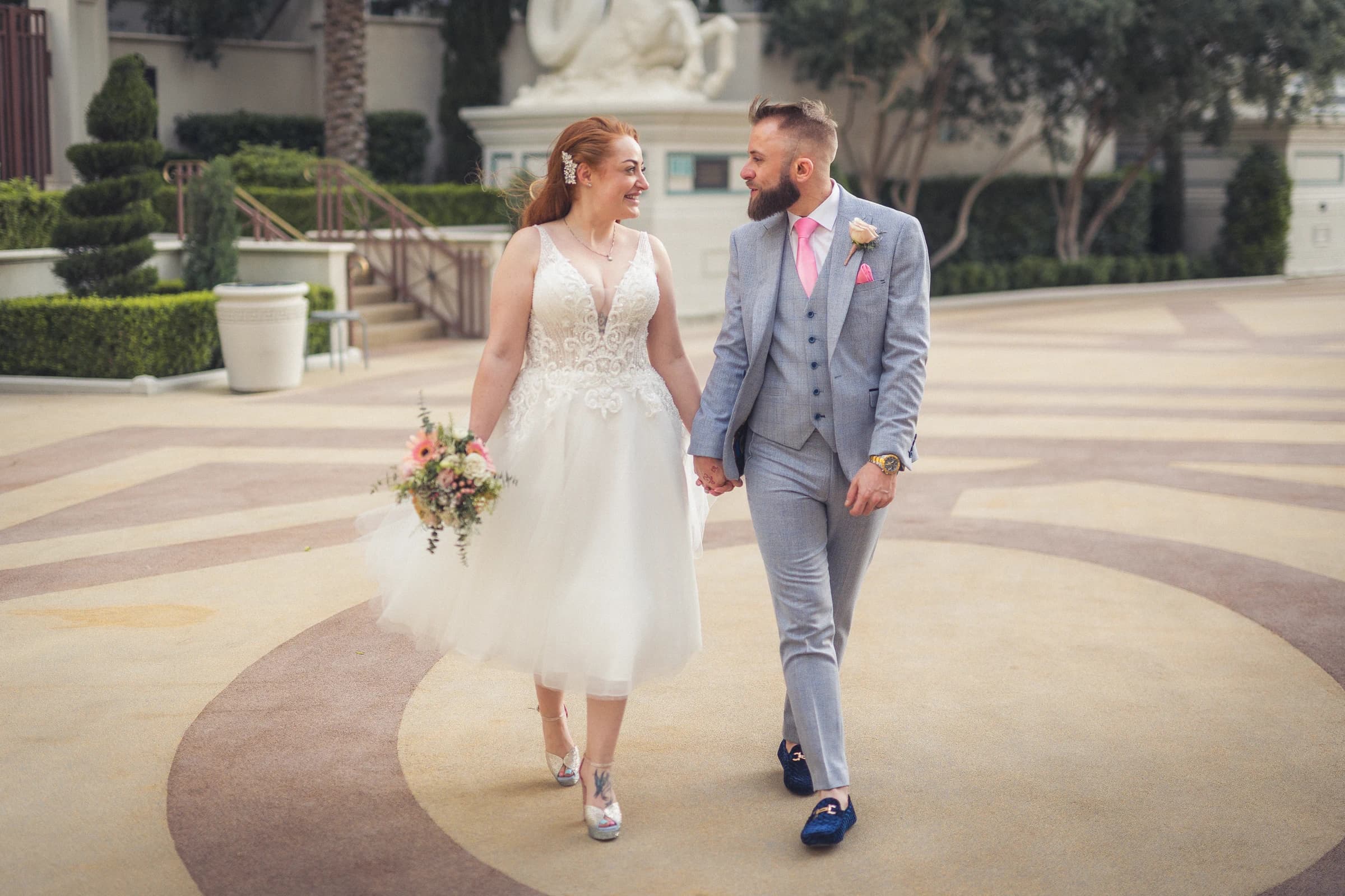 Newlyweds smile at each other while walking hand in hand across a patterned courtyard