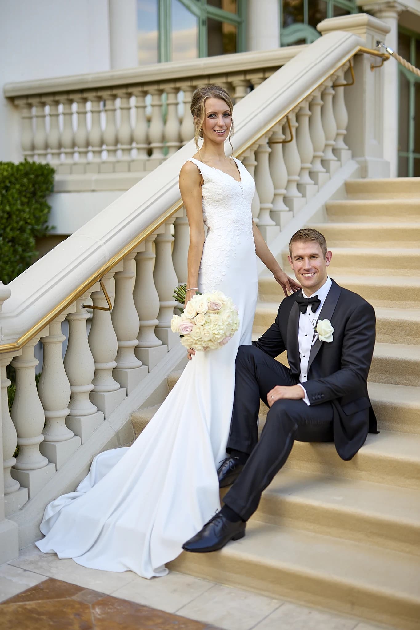 Newlyweds pose on an elegant staircase with the bride's bouquet